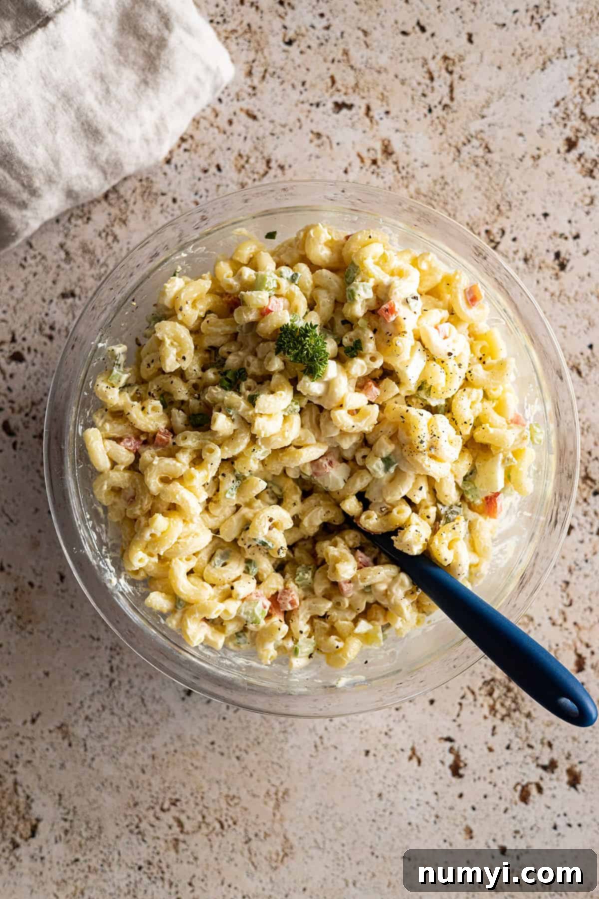 Overhead view of macaroni salad in a glass bowl with a dark spoon in the bowl. 