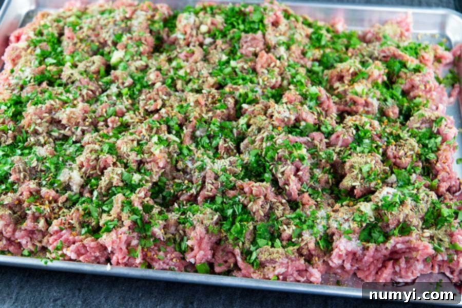 Authentic Homemade Fennel Italian Sausage Recipe 6 Ground pork sprinkled with various Italian sausage seasonings on a large baking sheet.
