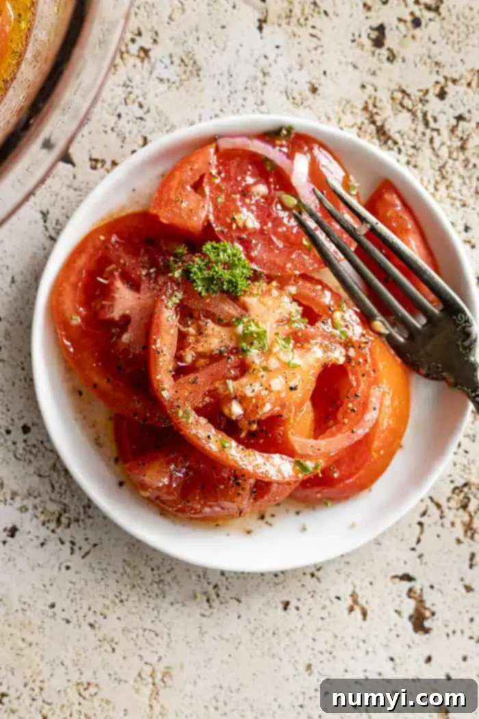 overhead closeup: marinated tomatoes on a white plate with a fork off to the side, garnished with fresh herbs