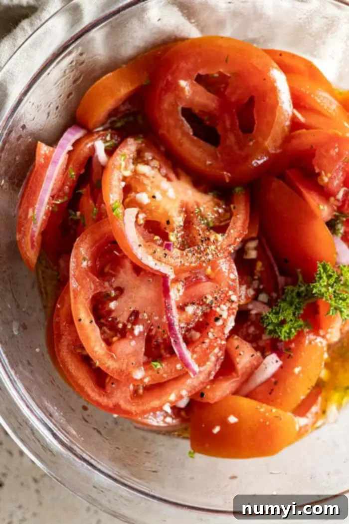 extreme closeup: my marinated tomato recipe in a bowl garnished with cracked pepper and flaky salt and fresh basil