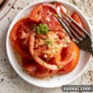 Marinated tomatoes on a white plate with a fork off to the side.