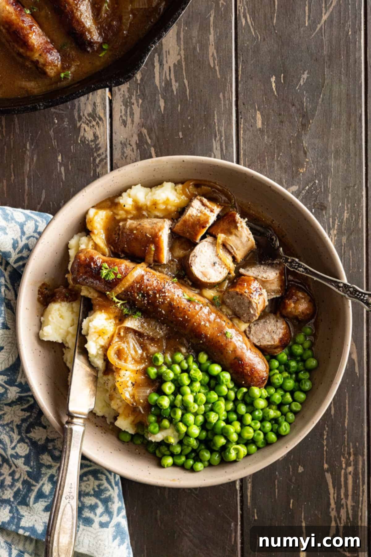 Overhead view of bangers and mash cut up on a plate with fork and knife on the plate ready to dive in.