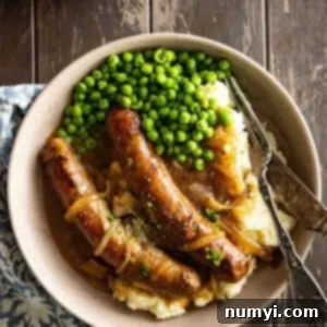 Overhead picture of bangers and mash on a plate with peas on the side.
