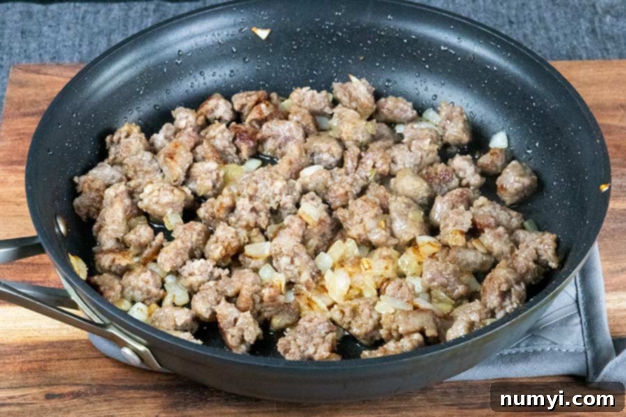 Sautéed sausage and chopped onions in a dark skillet, ready for the next step.