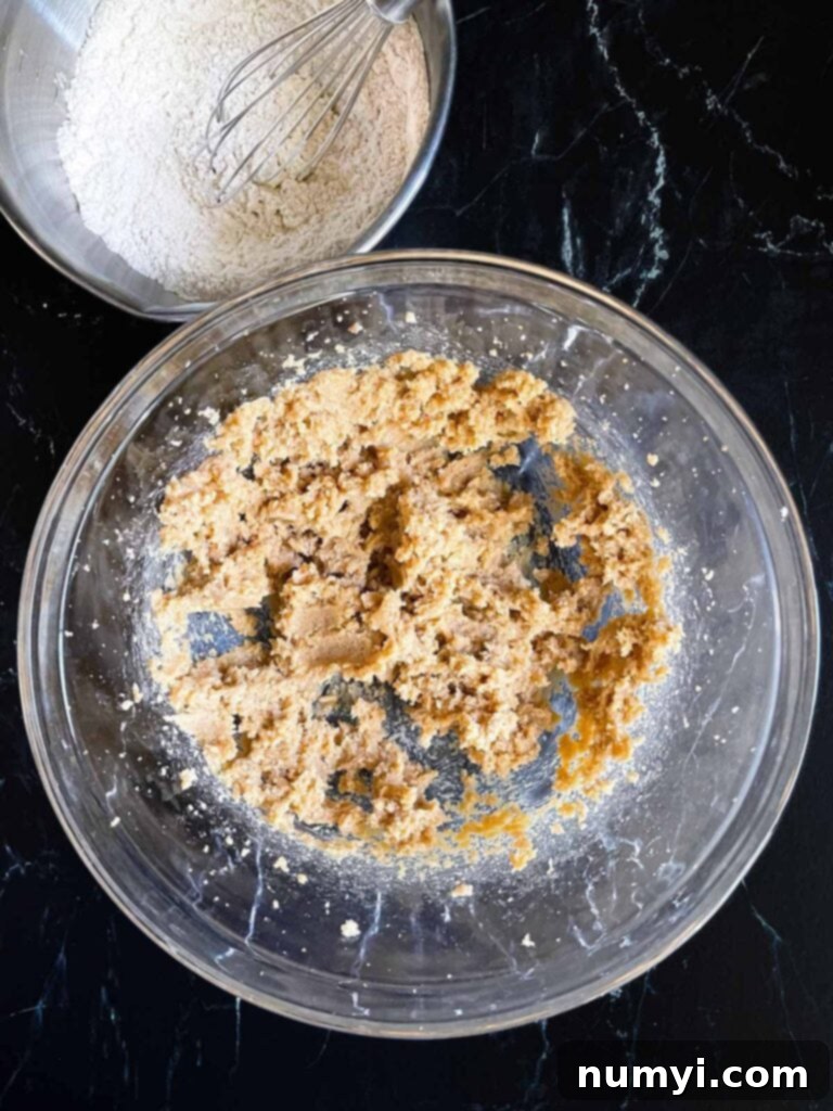 Butter and sugars creamed together for old fashioned oatmeal raisin cookies, creating a light and fluffy mixture in a clear glass bowl.