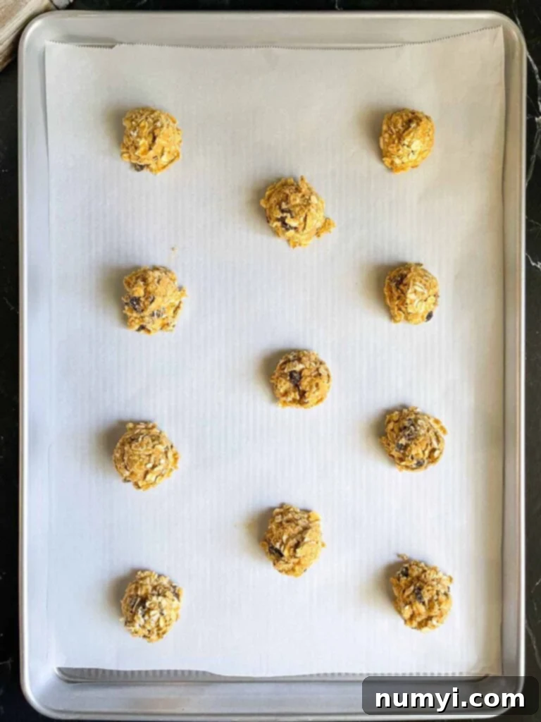 Uniformly sized old fashioned oatmeal raisin cookie dough balls neatly arranged on a parchment paper lined baking sheet, ready for baking.