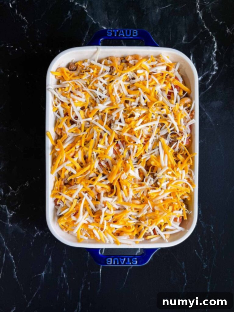 Beefaroni, topped with cheese in a blue casserole dish, about to go into the oven.