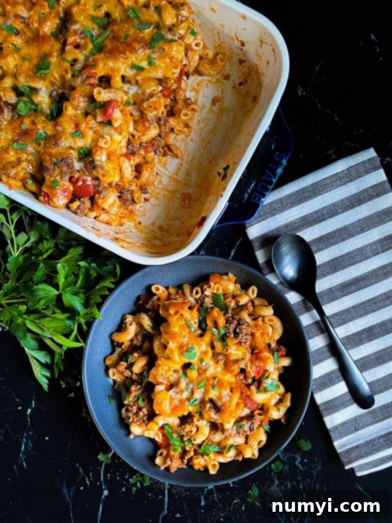 Cheesy beefaroni served in a dark bowl with the casserole off to the side.