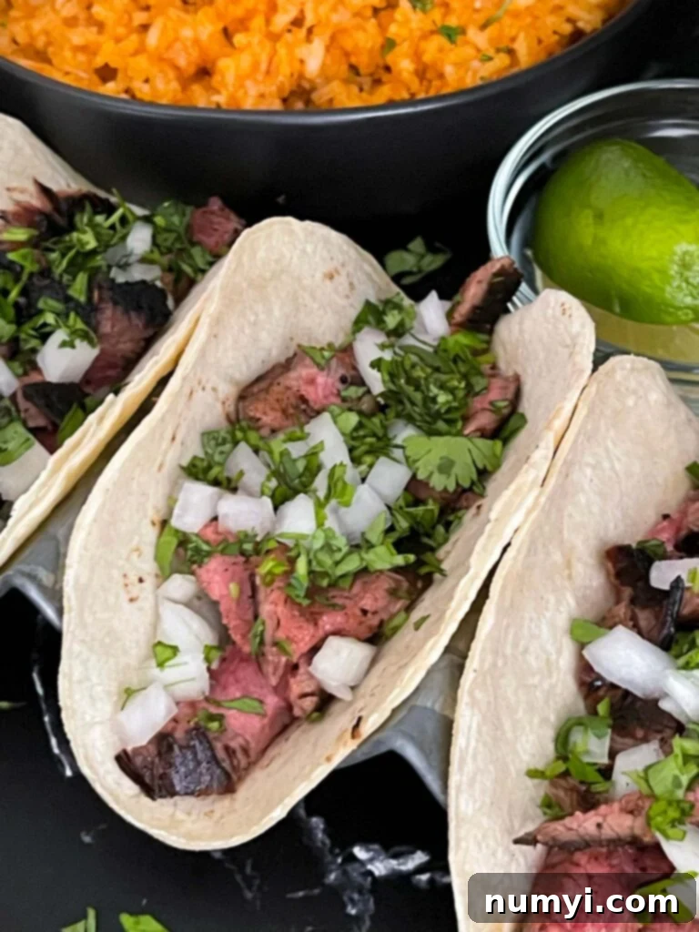 Flank steak street tacos with Mexican rice and fresh cilantro garnish on a dark background.