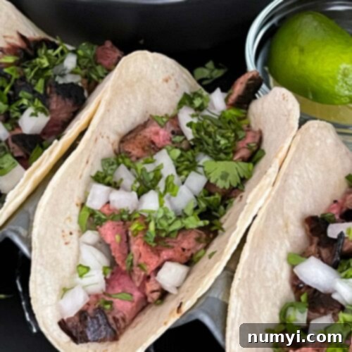 Flank steak street tacos with rice and garnish on a dark background.