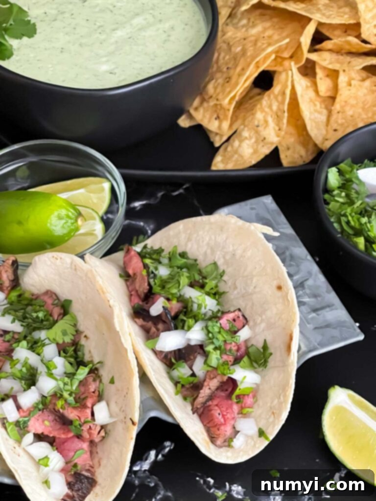Two authentic flank steak street tacos served with Mexican rice, tortilla chips, and fresh garnish on a dark background.