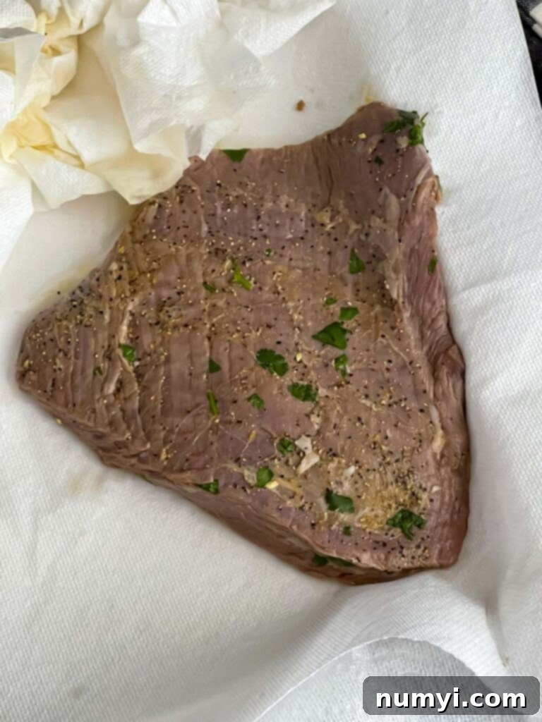 Marinated flank steak removed from the bag, ready to be grilled, showing its rich color and moisture.