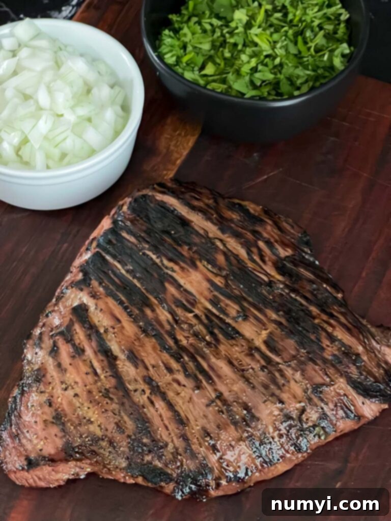 Perfectly grilled flank steak resting on a cutting board, alongside chopped onions and cilantro for topping.
