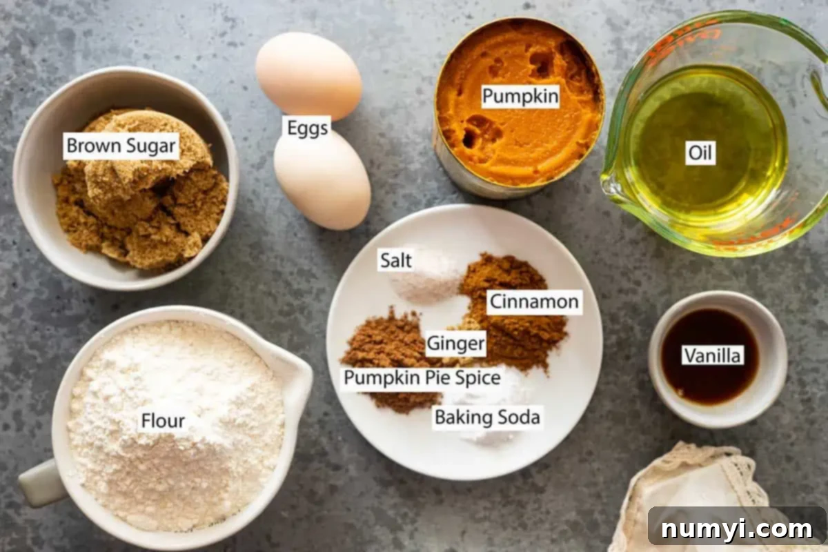 Ingredients for pumpkin muffins: pumpkin puree, oil, eggs, brown sugar, flour, cinnamon, ginger, pumpkin pie spice, salt, baking soda, and vanilla, neatly laid out.