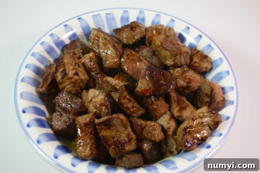 Browned cubed meat in a white bowl.