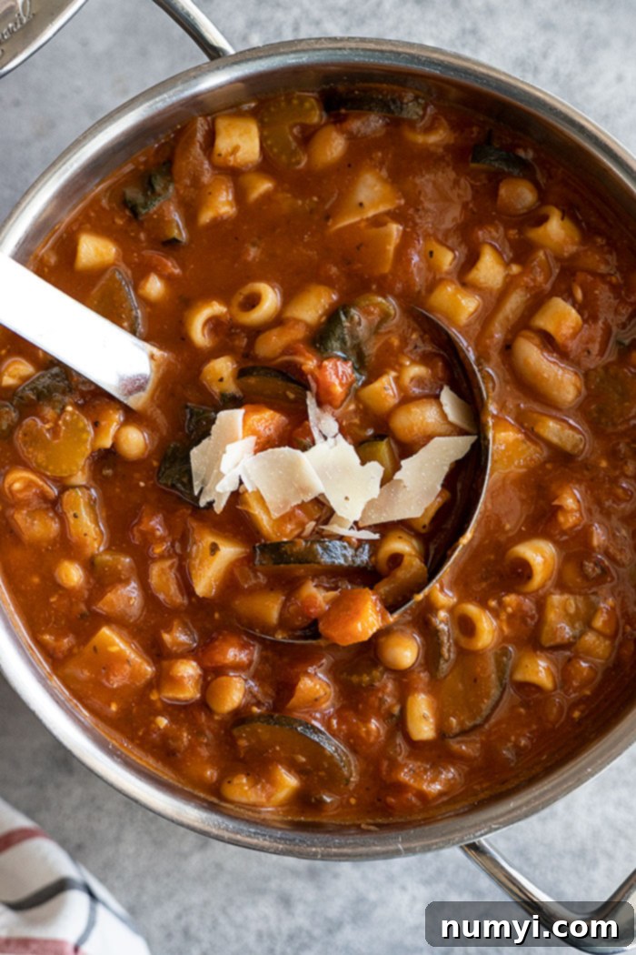 Overhead view of a pot of Minestrone soup with a soup ladle, garnished with fresh parmesan cheese and herbs, ready to be served.