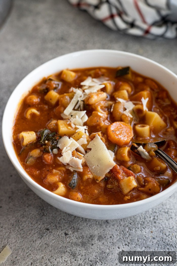 A serving of homemade minestrone soup in a white bowl, garnished with freshly grated parmesan cheese and a spoon, inviting a delicious bite.