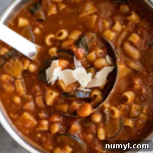 Overhead view of a pot of soup with soup ladle and garnished with parmesan cheese.