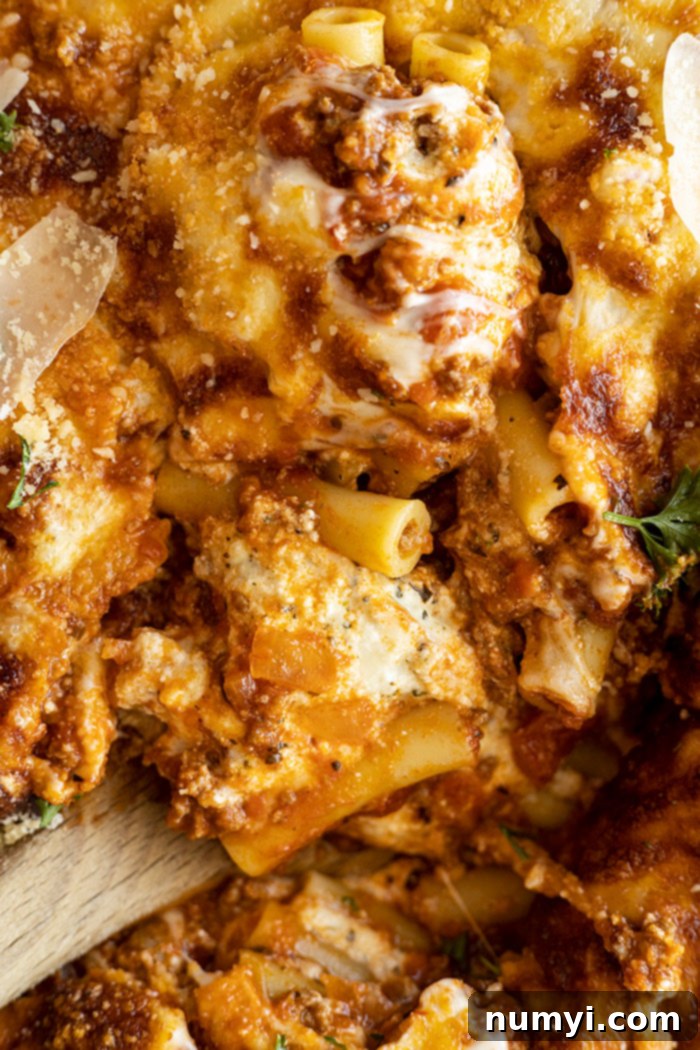Close-up view of a spoon digging into a baked ziti, revealing layers of pasta, meat sauce, and melted cheese, ready to be enjoyed.