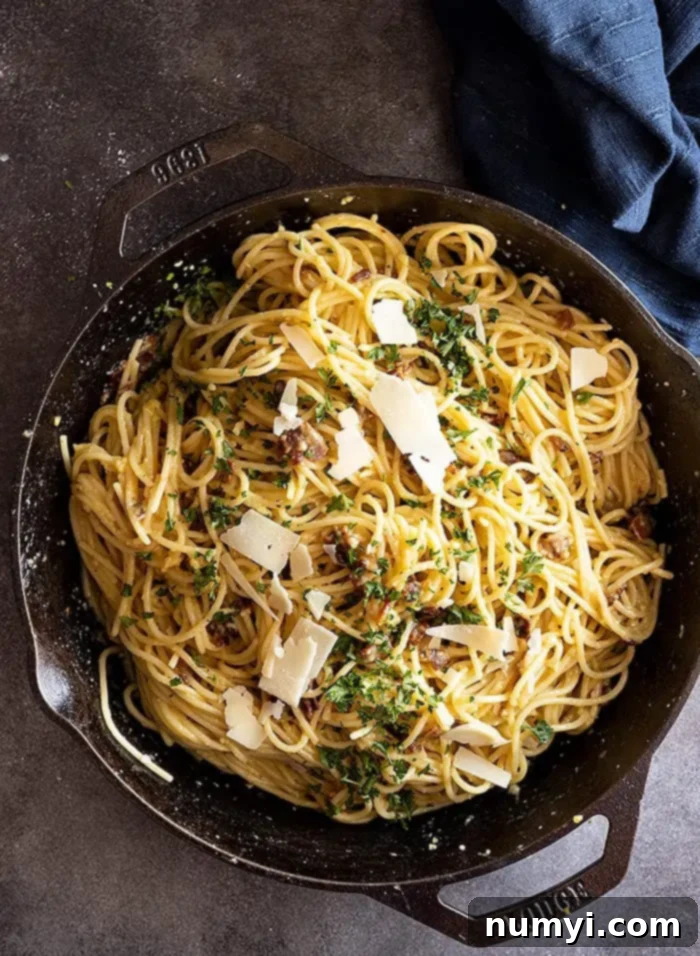 Overhead view of carbonara in a cast iron skillet garnished with parmesan and parsley. 