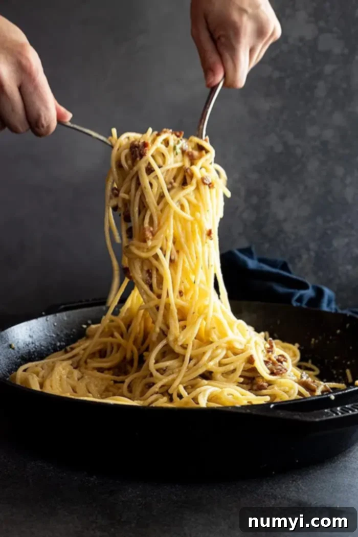 Two forks pulling up a generous portion of spaghetti carbonara ready to serve. 