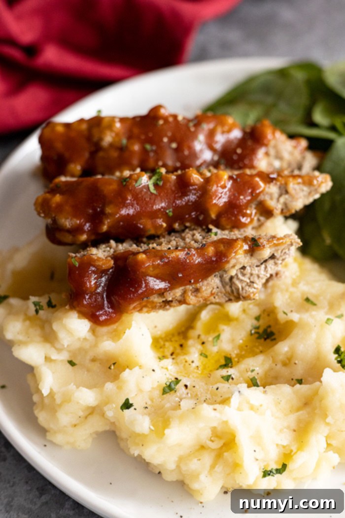 A close-up view of a perfectly glazed, tender Instant Pot meatloaf, sliced and artfully arranged over a bed of creamy mashed potatoes on a white plate, highlighting its delicious texture and rich flavor.