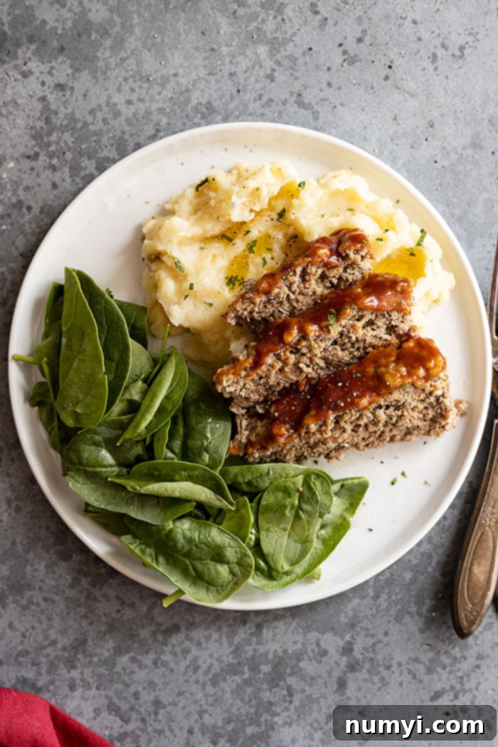 An inviting overhead shot of Instant Pot Meatloaf and Mashed Potatoes presented on a clean white plate, with a fork and a rustic red napkin positioned elegantly to the side.