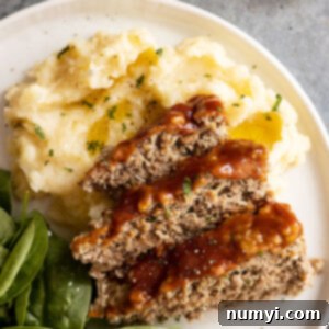 Meatloaf and mashed potatoes on a white plate. Mashed potatoes garnished with fresh parsley and pepper.