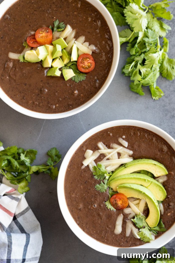Hearty Black Bean Soup 5 Two bowls of soup garnished with cheese, avocado, and cilantro. Bunches of cilantro in the corner of the picture.