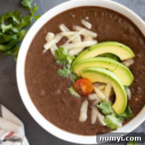 Hearty Black Bean Soup 6 Overhead view of black bean soup in a white bowl garnished with avocado, cheese, cilantro, and tomato.