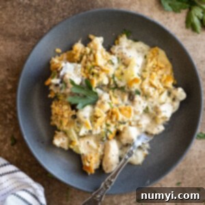 Overhead view of poppy seed chicken casserole on a dark blue plate with a fork. Garnished with fresh parsley and black pepper.