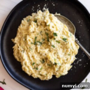 Orzo served on a black plate with a spoon ready to take a bite. Garnished with fresh parsley , parmesan cheese, and black pepper.