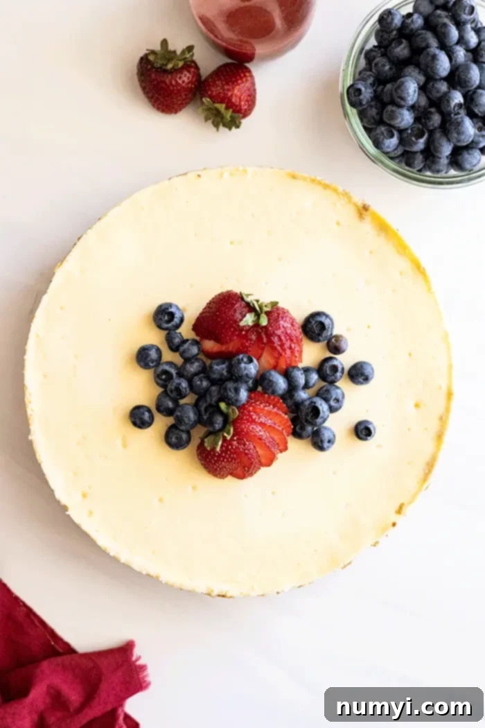 Overhead view of finished whole cheesecake with blueberries and sliced strawberries on top.