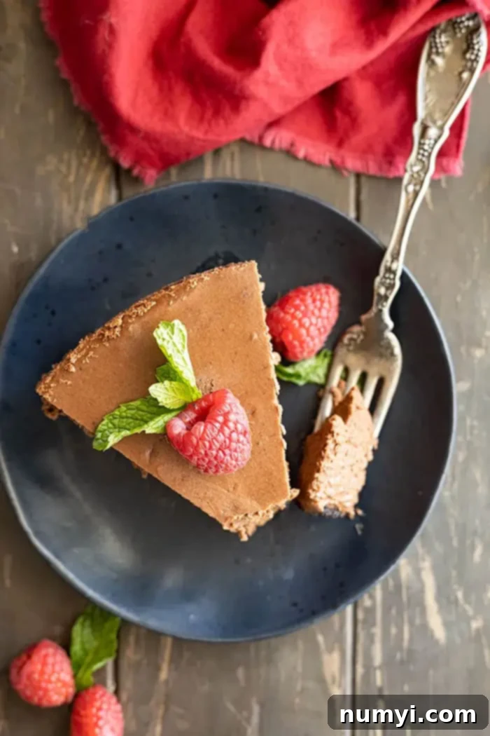 overhead: slice of chocolate cheesecake topped with raspberry and mint leaves on a plate with fork