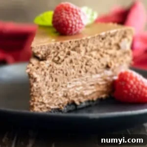 Slice of chocolate cheesecake on a black plate with a raspberry and mint for garnish.