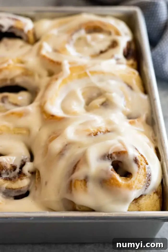 A close-up view of a pan filled with freshly baked cinnamon rolls, generously covered in a luscious cream cheese frosting, ready to be served.
