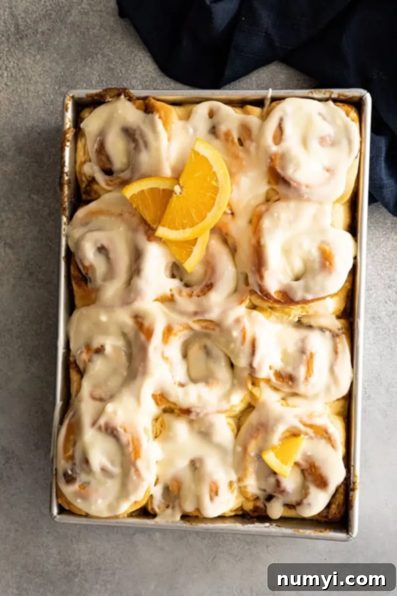 Zesty Orange Cinnamon Rolls 2 Overhead view of orange cinnamon rolls topped with cream cheese frosting and a couple orange slices for garnish.