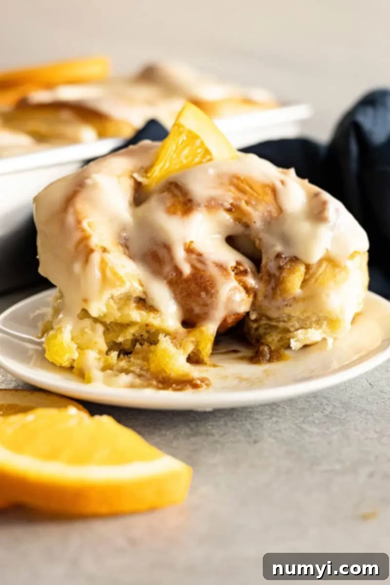 Zesty Orange Cinnamon Rolls 7 A roll on a white plate with a bite taken out. Small piece of orange on top for garnish.