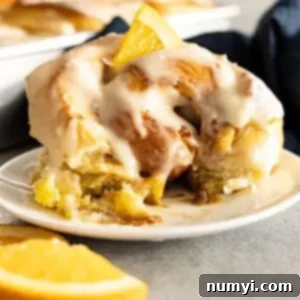 Zesty Orange Cinnamon Rolls 8 A roll on a white plate with a bite taken out. Small piece of orange on top for garnish.