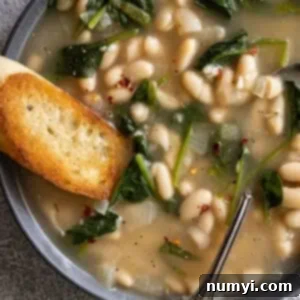 Close up of soup in a bowl. Piece of crusty garlic bread dunking into the soup.