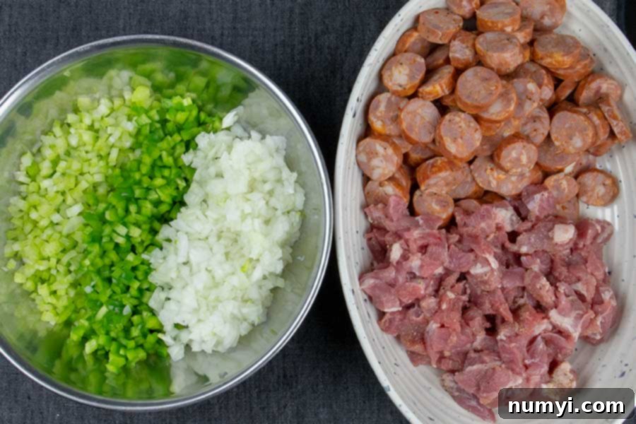 Prepped ingredients: finely diced celery, bell pepper, and onions in one bowl, and separately, diced pork and sliced Andouille sausage in another.