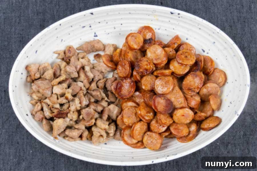 Perfectly browned pork and sliced Andouille sausage in a white serving bowl, ready to be added back to the jambalaya.