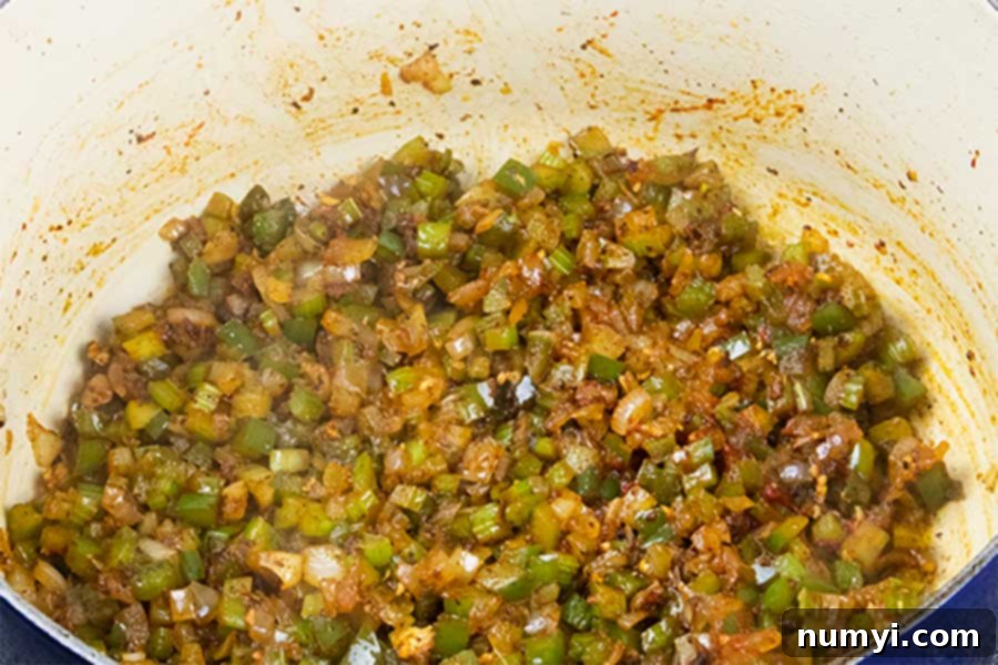 The Holy Trinity (diced onions, celery, and bell pepper) along with garlic and tomato paste cooking in a large Dutch oven, creating a rich base for jambalaya.
