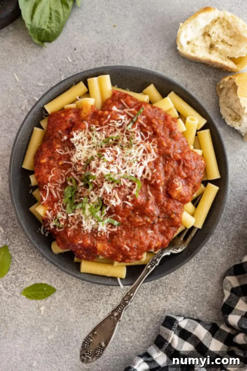 Overhead view of homemade marinara sauce on a bed of spaghetti pasta, garnished with fresh basil and grated Parmesan cheese.