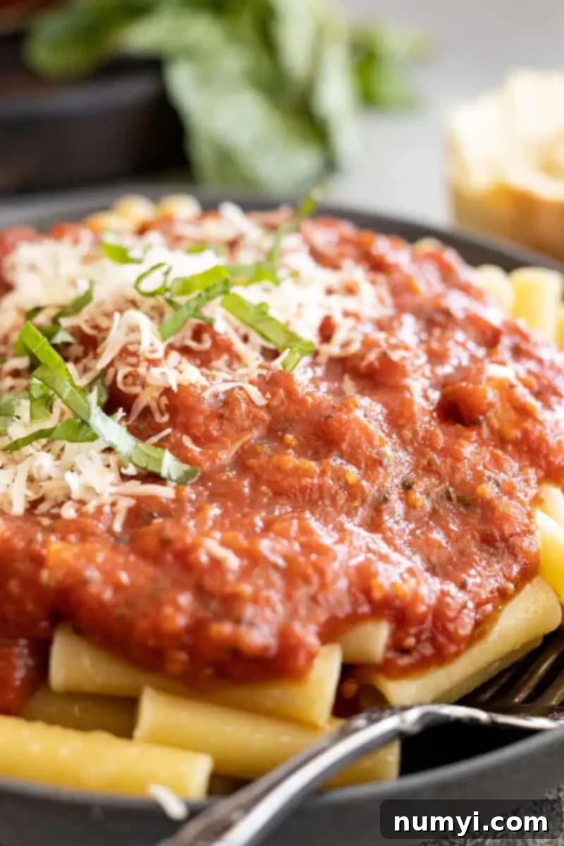 Close up of marinara sauce generously coating pasta on a dark plate, with a fork to the side, highlighting the rich texture.