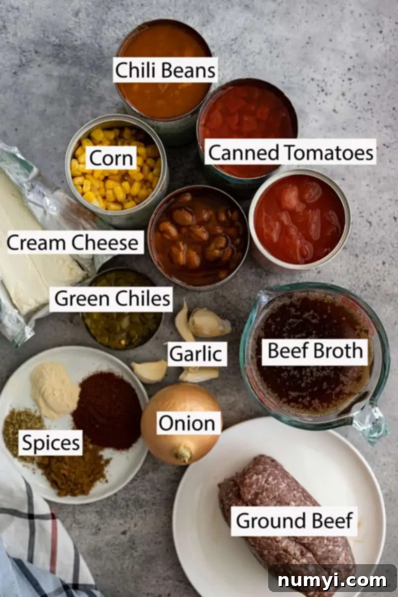 A selection of essential ingredients laid out for making creamy taco soup: Canned diced tomatoes, two cans of chili beans, a can of corn, a block of cream cheese, a can of chopped green chiles, beef broth, ground beef, and various taco-inspired spices including cumin, chili powder, and oregano.
