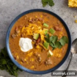 Overhead view of a bowl of creamy taco soup garnished with sour cream, avocado, cilantro, and grated cheddar.