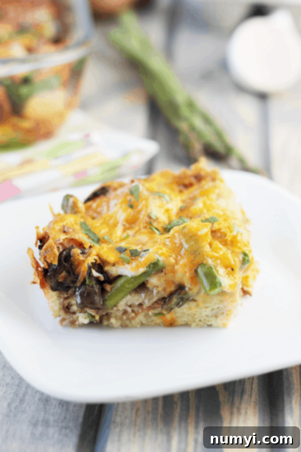 A perfectly baked slice of mushroom and asparagus strata on a white plate, showcasing its golden crust and delicious layers.