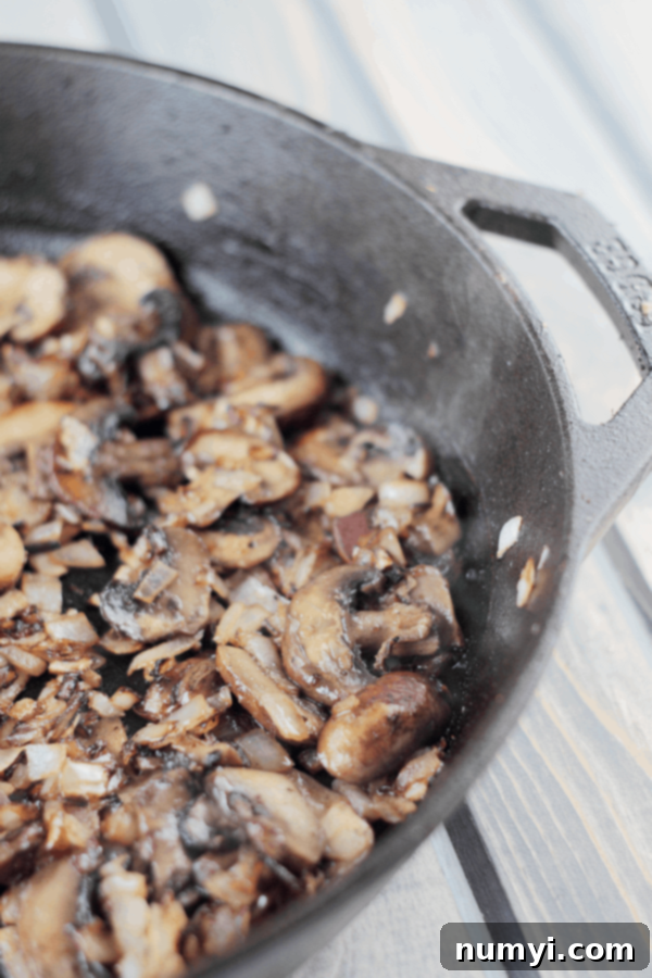 Sautéed mushrooms and onions simmering in a cast iron pan, ready to be added to the strata layers.