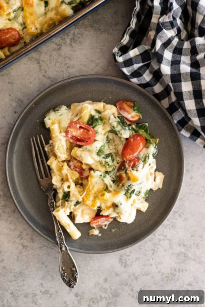 Overhead shot of a creamy Chicken Florentine Pasta Casserole on a dark plate with a fork, garnished with fresh herbs, ready to be served.